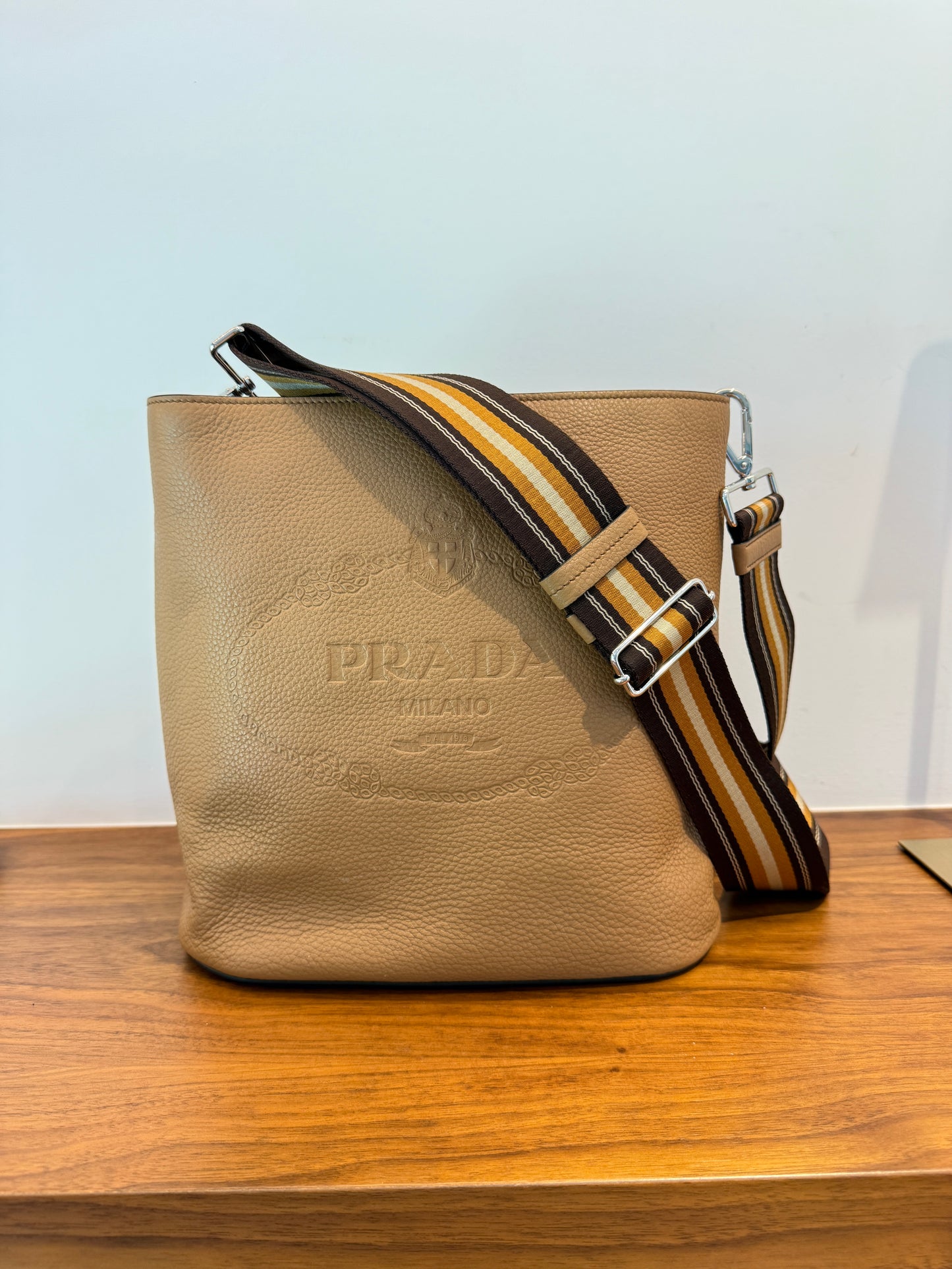 A Prada beige leather bucket bag with a wide striped webbing shoulder strap, authentic, pre-owned and for sale from purseonalshopper