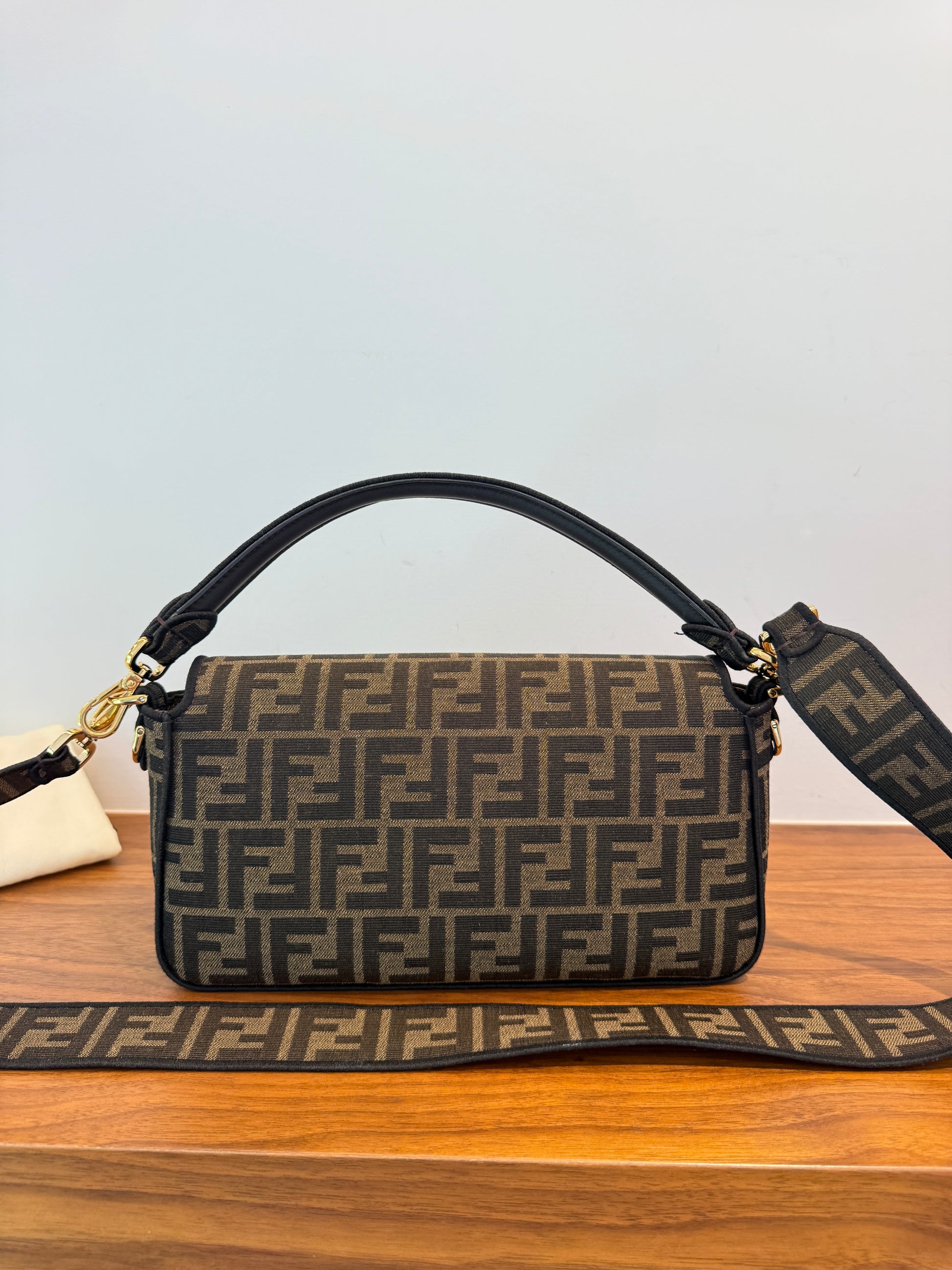 A Fendi handbag in brown and beige Zucca monogram canvas with a black leather top handle and a matching monogram shoulder strap back side is shown in photo