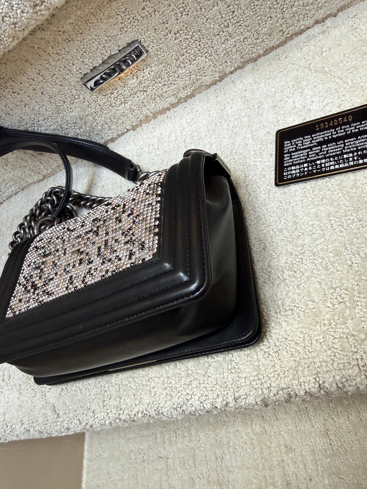 Black chanel handbag with decorative chain strap on a textured beige surface with black card