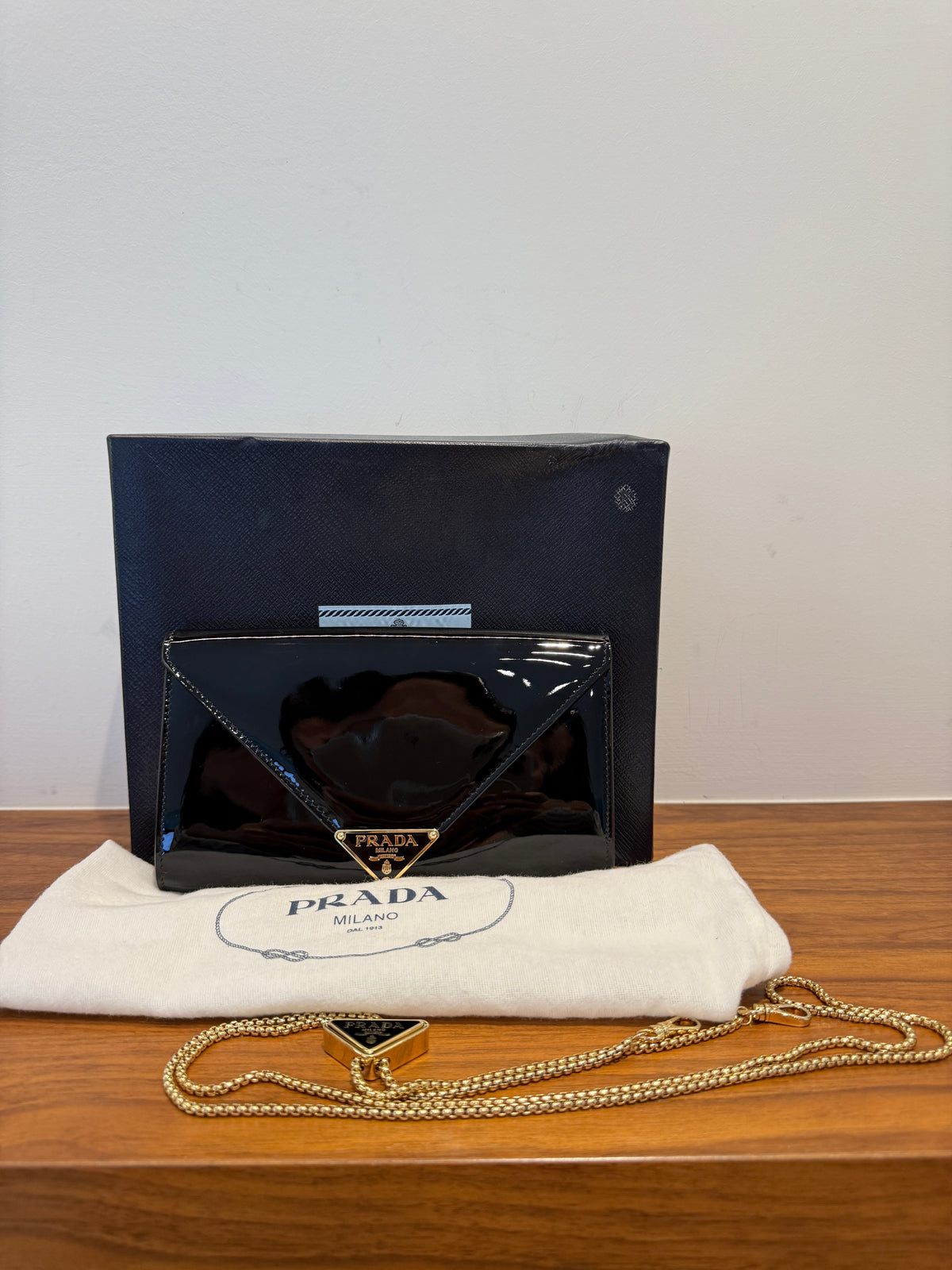 Prada envelope clutch in glossy black patent leather with a gold-tone triangle logo and an adjustable gold chain strap with a metal triangle.  authentic and preowned.