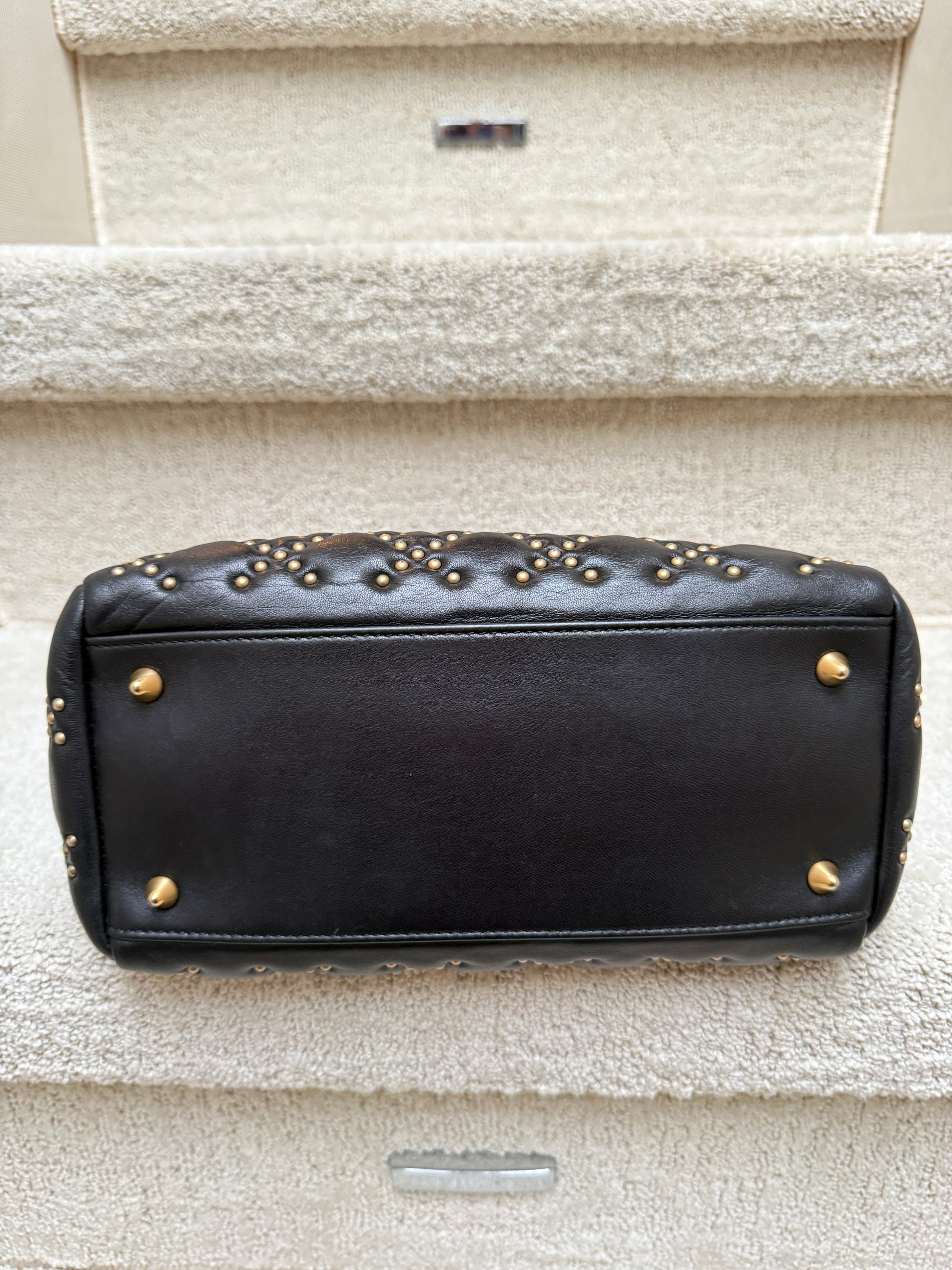 Lady Dior in size medium black leather with gold studs showing bottom of bag with feet